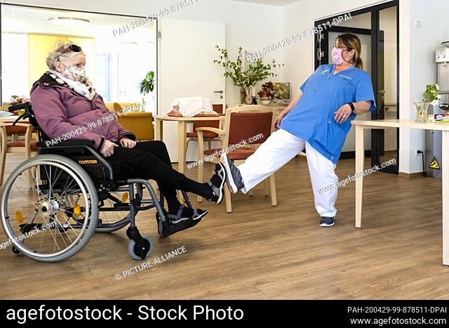 24 April 2020, Schleswig-Holstein, Kiel: Geriatric nurse Jaqueline Ackermann (r) and resident Karin Plagemann welcome each other by foot in the Kurt-Engert-Haus...