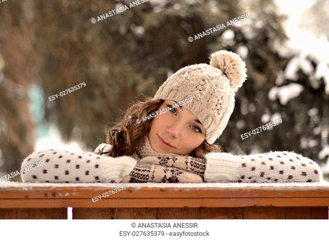 Very beautiful, pretty girl with hat, sweater, warm mittens, curly, brown hair in winter, snowbound forest look, you, curl up, put head on hands, put hands