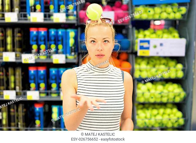 Beautiful caucasian woman shopping sports equipment in sportswear store. Lady throwing tennis ball in the air