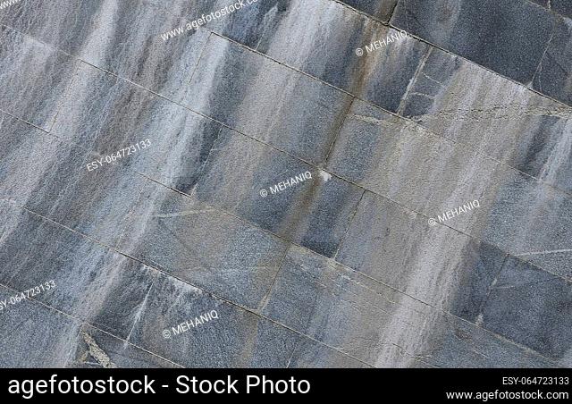 The texture of a wall of large granite tiles that are covered with white streaks when exposed to dampness