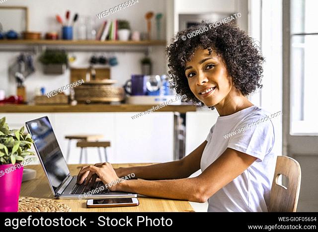 Portrait of smiling woman using laptop at table at home