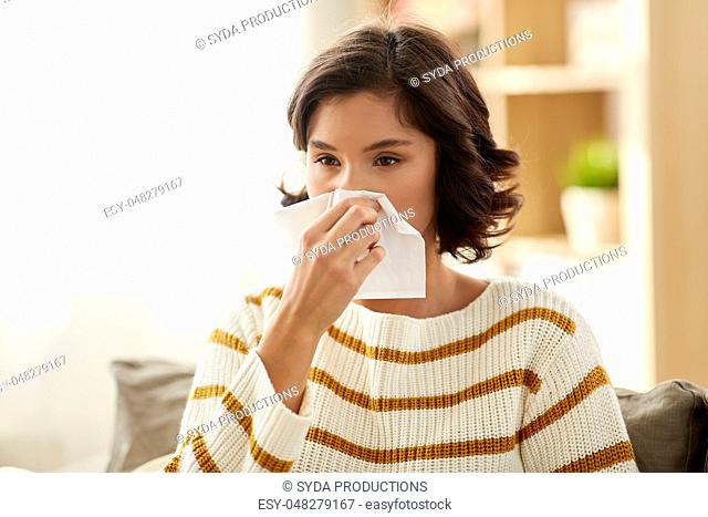 sick woman blowing nose in paper tissue at home