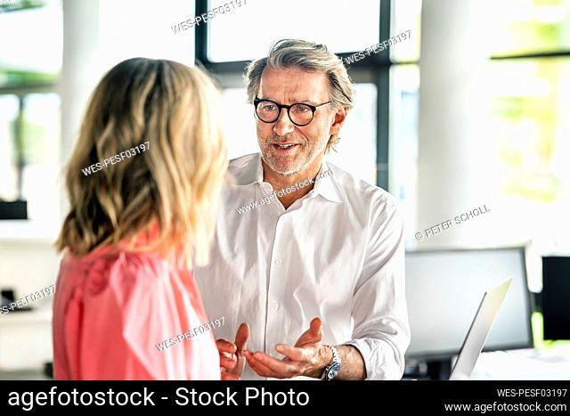 Businessman wearing eyeglasses gesturing with female professional in office
