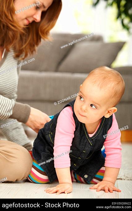 Baby girl crawling on floor with mum sitting in the background