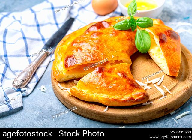 Traditional closed pie with cheese and egg in the shape of a crescent cut into pieces on a wooden serving board, selective focus