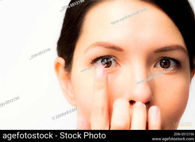 Woman about to place a disposable plastic contact lens in her eye to correct her vision has it balanced on the end of her finger in front of her face with focus...