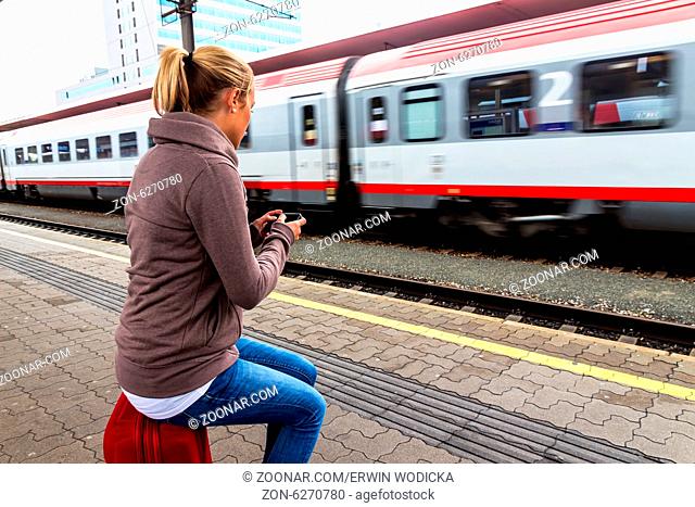 Eine junge Frau wartet auf einen Zug und schreibt mit ihrem Handy ein SMS