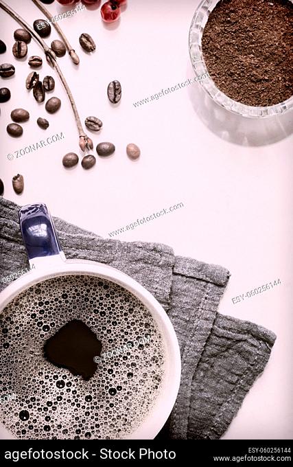 On the table on a napkin is a Cup of black coffee, next to coffee beans and freshly ground black coffee. Top view, close-up