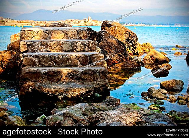 Old tower stone stairs isolated in blue sea water background with rocks and mountain
