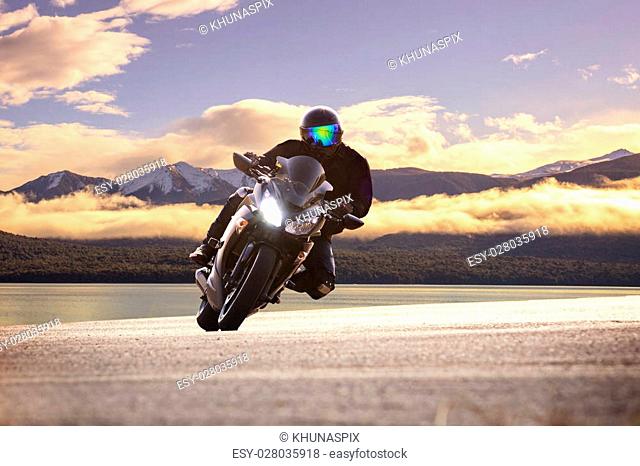 young man riding big bike motorcycle against sharp curve of asphalt high ways road with rural lake scene use for male adventure activities and motor sport hobby...