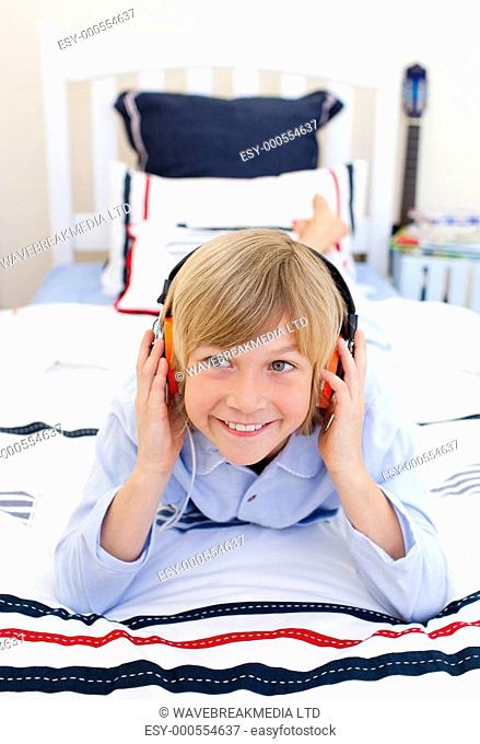 Relaxed boy listening music lying down on bed with headphones