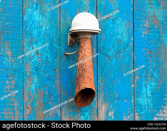 Rusty alarm horn hanging on a blue wall