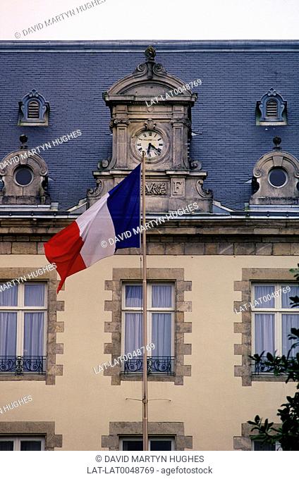 Close-up of French flag outside building with clock. Cream walls. Tiled roof. Vendee region