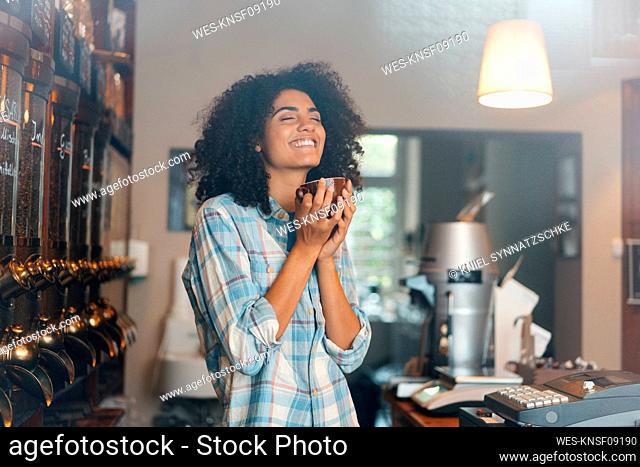 Happy owner with eyes closed smelling roasted coffee in cup at store