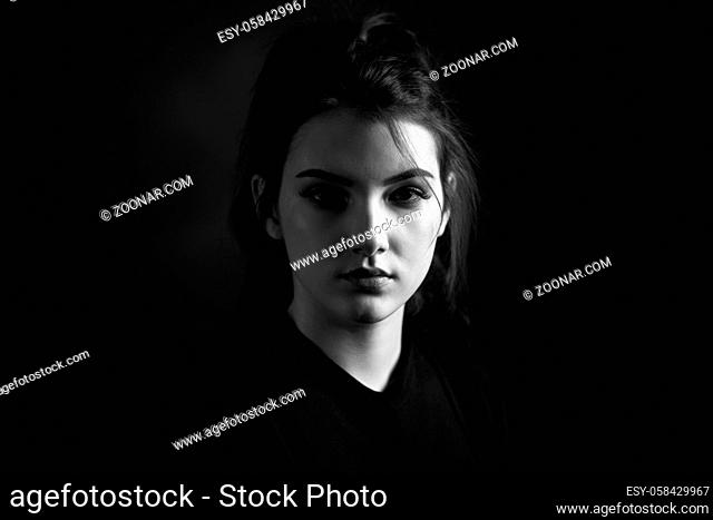 Dramatic black and white portrait of a beautiful lonely girl on a dark background in studio