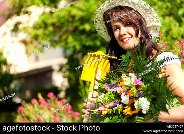 Gardening in summer - happy woman with flowers and hat in her garden