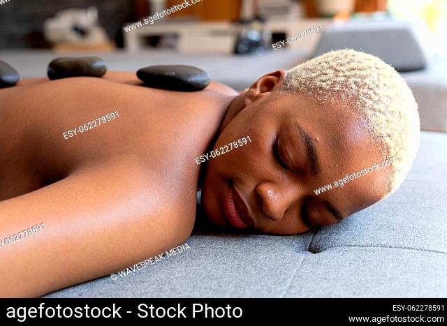 Happy african american woman lying with hot stones on her back