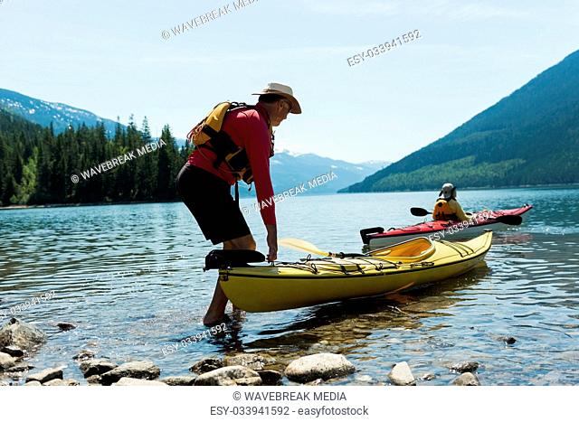 Man holding kayak while woman kayaking in lake