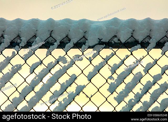 A close up soft focus shot of a chain link fence, aka diamond mesh, hurricane fencing, wire netting boundary, covered with snow during golden hour