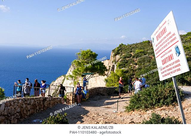01.10.2018, Greece, Zakynthos: A warning sign ""Caution!"" stands on the steep coast of Navagio Bay on the Greek island of Zakynthos