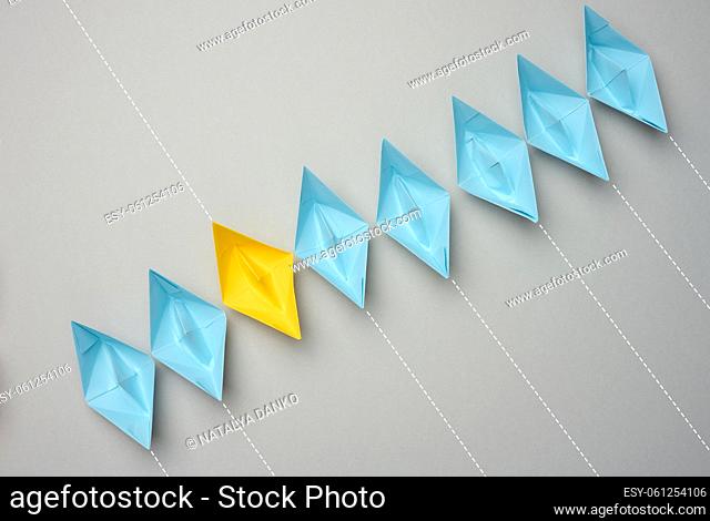 A row of paper boats on a gray background, yellow is moving in the opposite direction. Uniqueness of personality, individuality and independence from another...