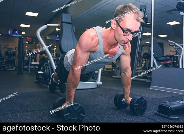 Strong man doing push-ups exercises on dumbbells