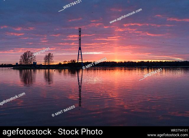 A view of a tall mast and buildings on the coastline of islands near Helsinki, at sunset