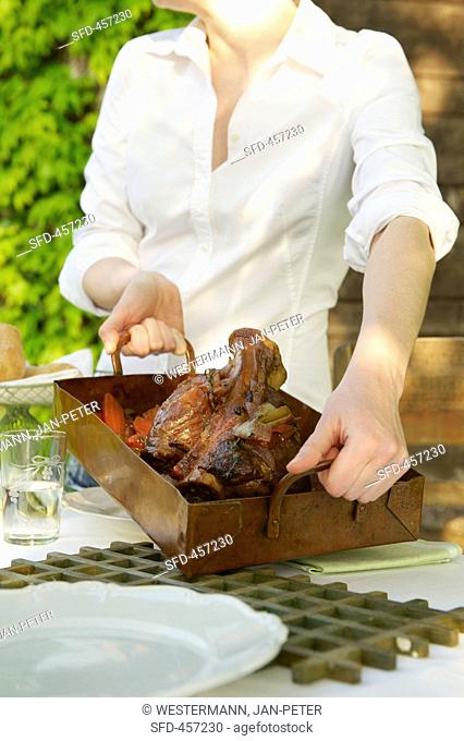 A woman holding a roast veal knuckle in a roasting tin