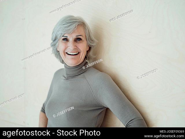 Happy senior woman with gray hair standing in front of wall