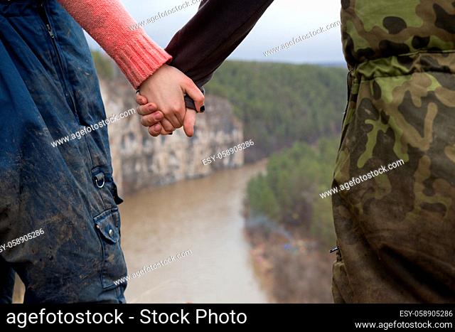 Hands of young couple hikers standing on the edge of a cliff over the mountain river, telephoto shot