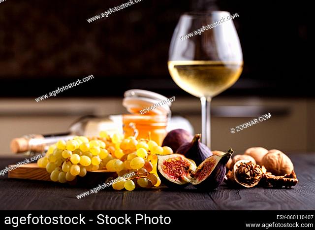 Grape, figs and honey with a glasses of white wine on wood background