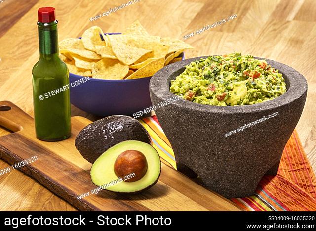 Guacamole and Chips with a green hot sauce in a bottle
