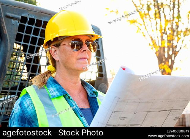 Female Worker Holding Technical Blueprints Near Small Bulldozer At Constrcution Site