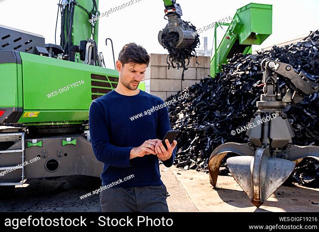 Businessman using smart phone in front of excavator