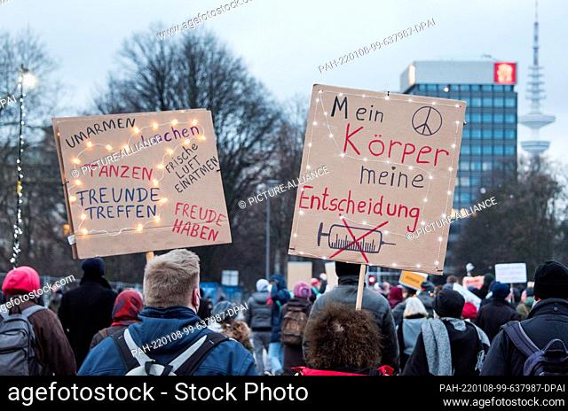08 January 2022, Hamburg: Participants in a demonstration against Corona restrictions march through the city center holding up placards reading ""Hug, laugh
