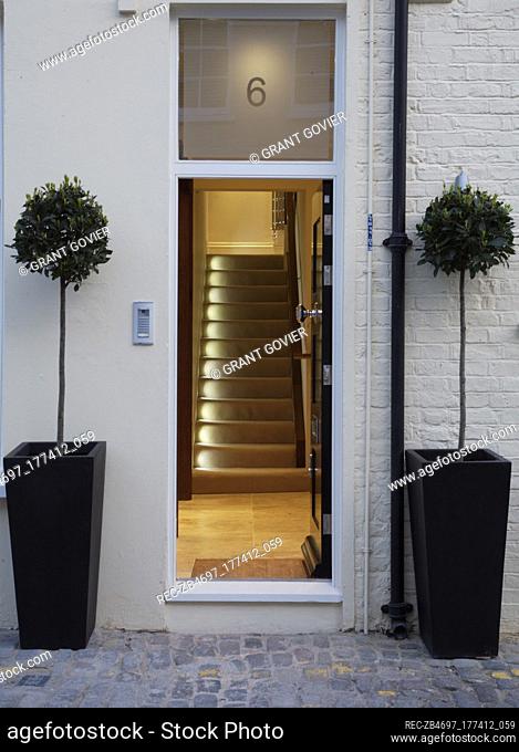 Front door flanked by two potted bay trees with a view through to illuminated staircase