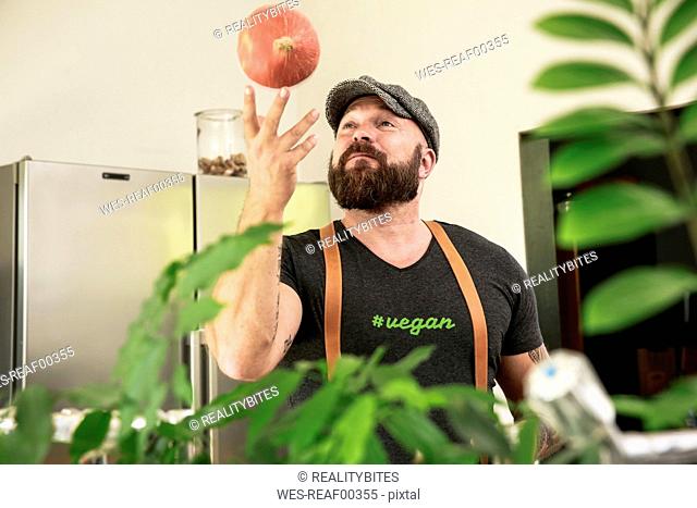 Vegan man playing with a pumpkin in his kitchen