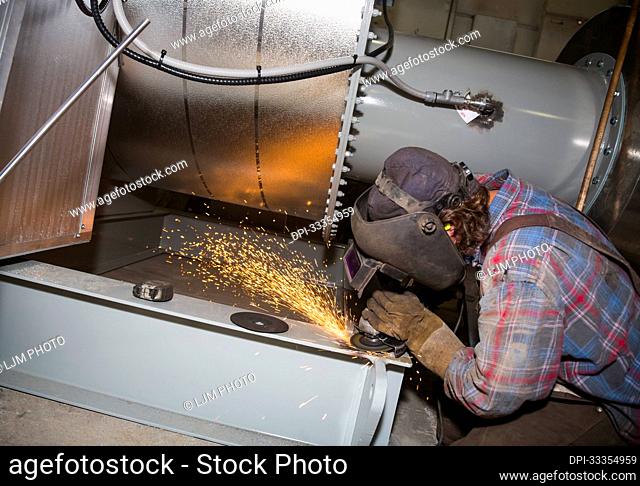 Tradesman grinding a welding seam on a unit that was fabricated in a plant; Innisfail, Alberta, Canada