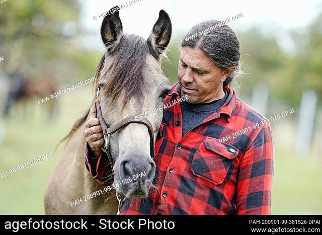 31 August 2020, Baden-Wuerttemberg, -: Dominic Sohl, tenant of a horse farm in the Heidelberg area, is standing with a horse in a pasture