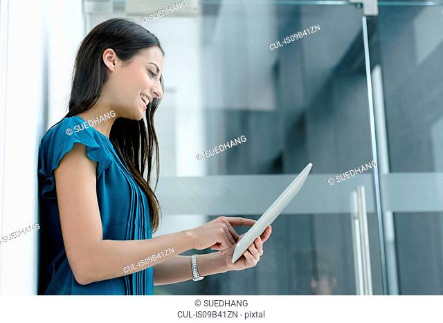 Window view of young businesswoman using digital tablet touchscreen at office entrance