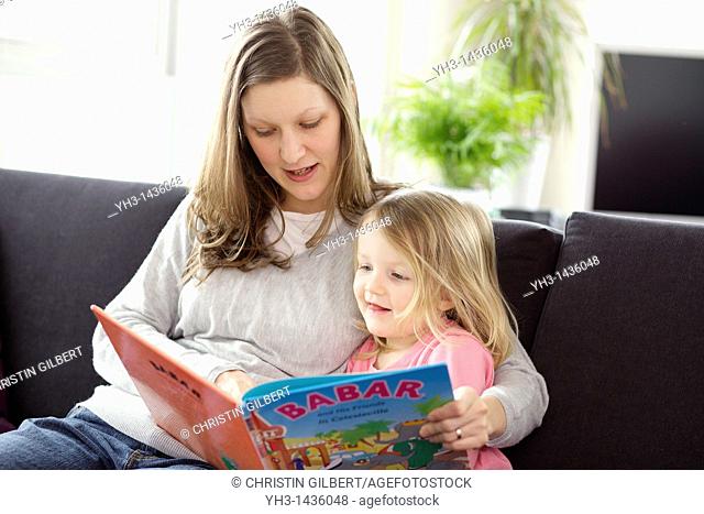 Young mother reading children book to his three year old daughter in the living room