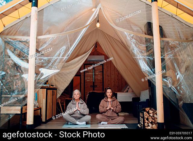 Woman senior and young relaxing at glamping camping tent. Women family elderly grandmother and young granddaughter doing yoga and meditation indoor