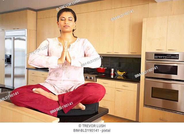 Indian woman meditating in kitchen