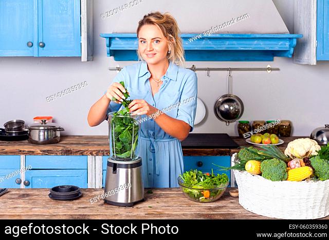 Happy woman putting ingredients into blender to make healthy smoothie for breakfast, cooking vegetables preparing salad in modern kitchen, raw food diet