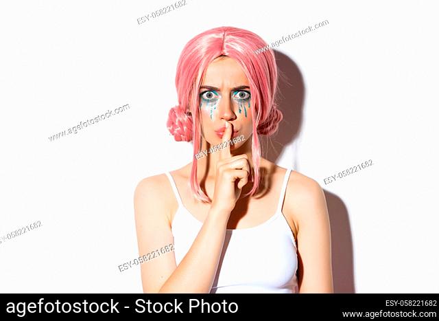 Close-up of angry girl with pink wig, frowning and shushing with mad face, standing over white background