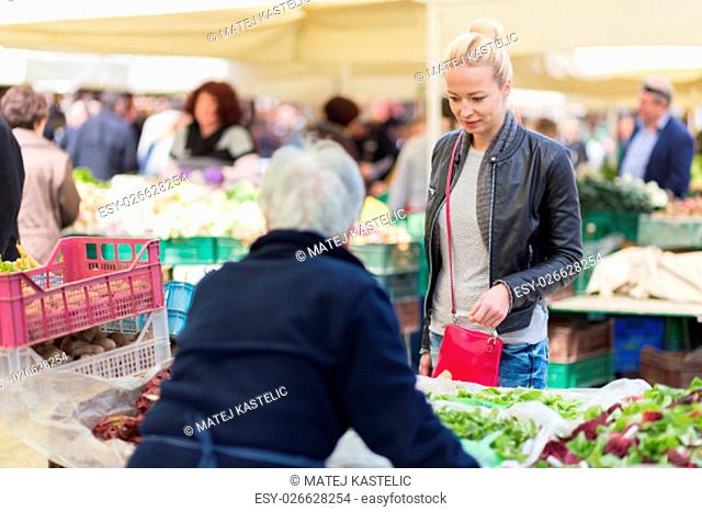 Woman buying fruits and vegetables at local food market. Market stall with variety of organic vegetable