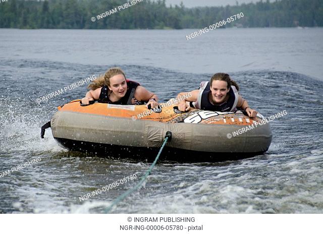 Portrait of two girls lying on an inflatable raft floating in a lake, Lake Of The Woods, Ontario, Canada