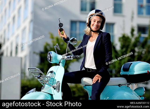 Businesswoman holding sunglasses while sitting on motor scooter