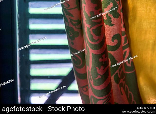 Still life, summer mood, shutter made of slats protects against heat, red wall hangings, golden wall