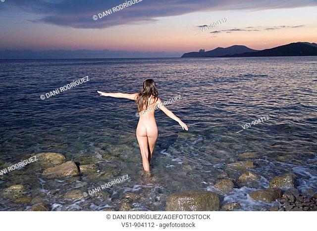 Naked woman walking on the beach at sunset